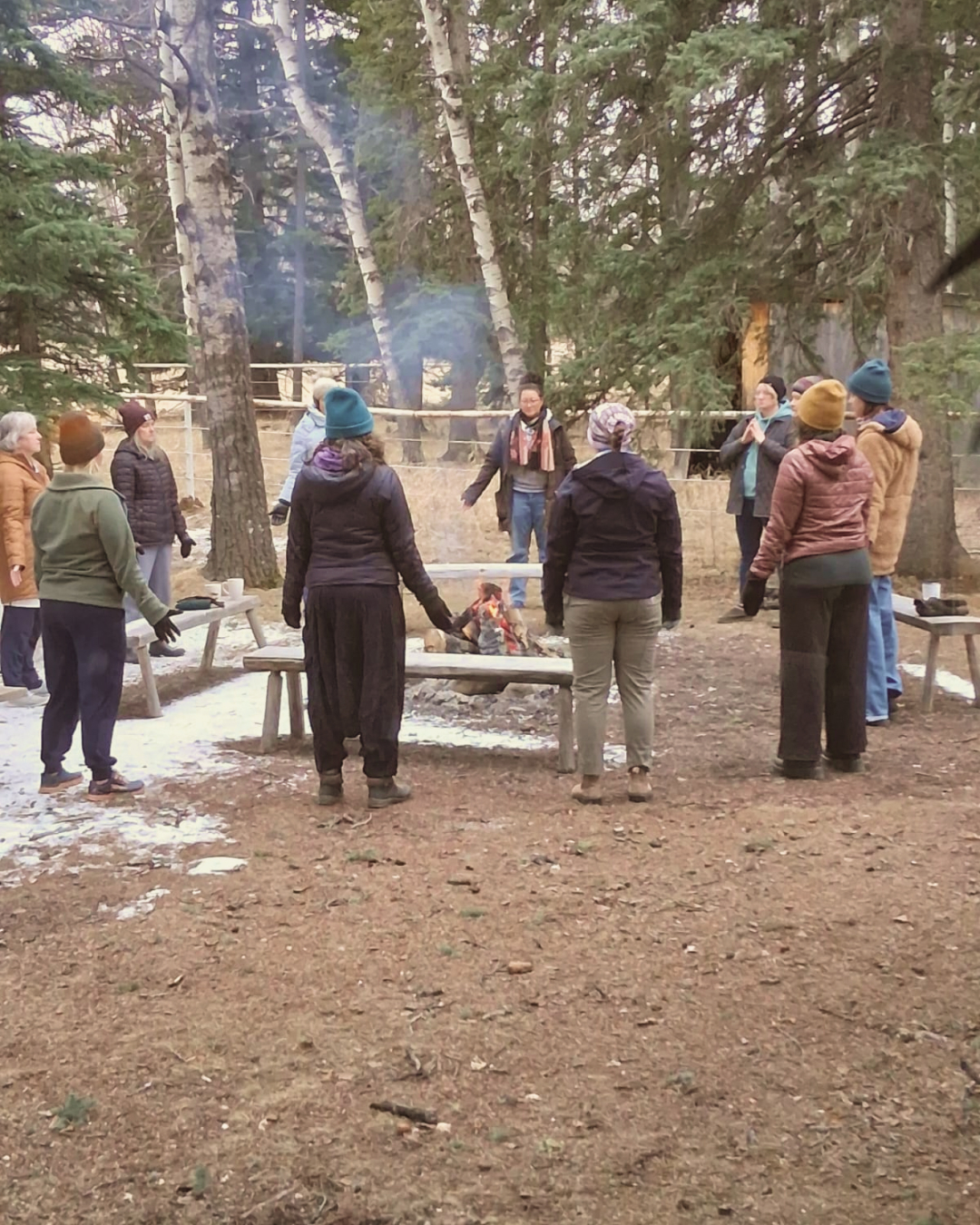 The group standing in a circle around a small fire in the trees in the morning