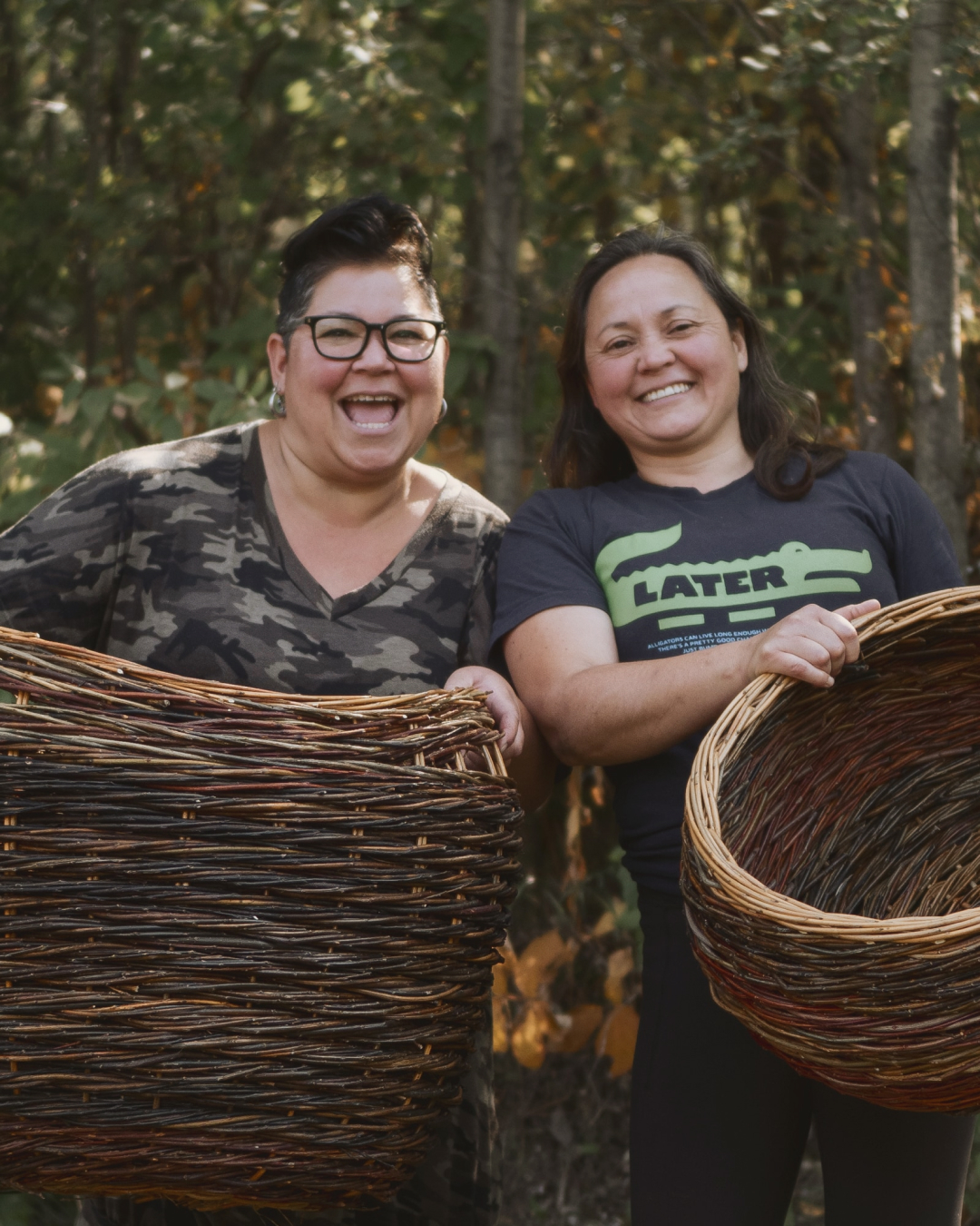 Two weavers laughing together, each holding a large finished willow basket