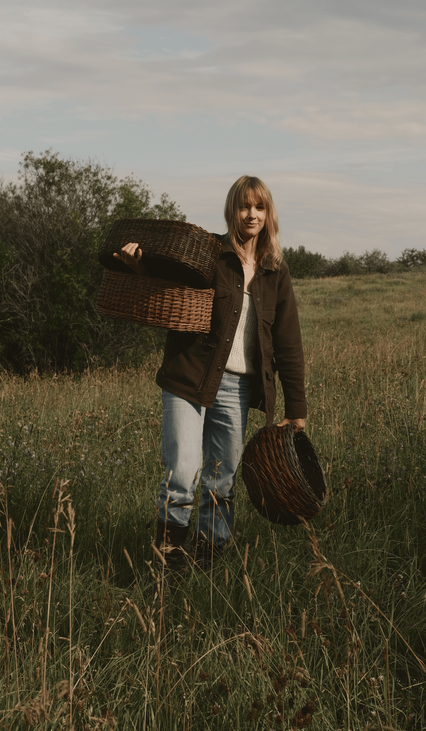 A weaver carrying freshly made willow baskets across a field