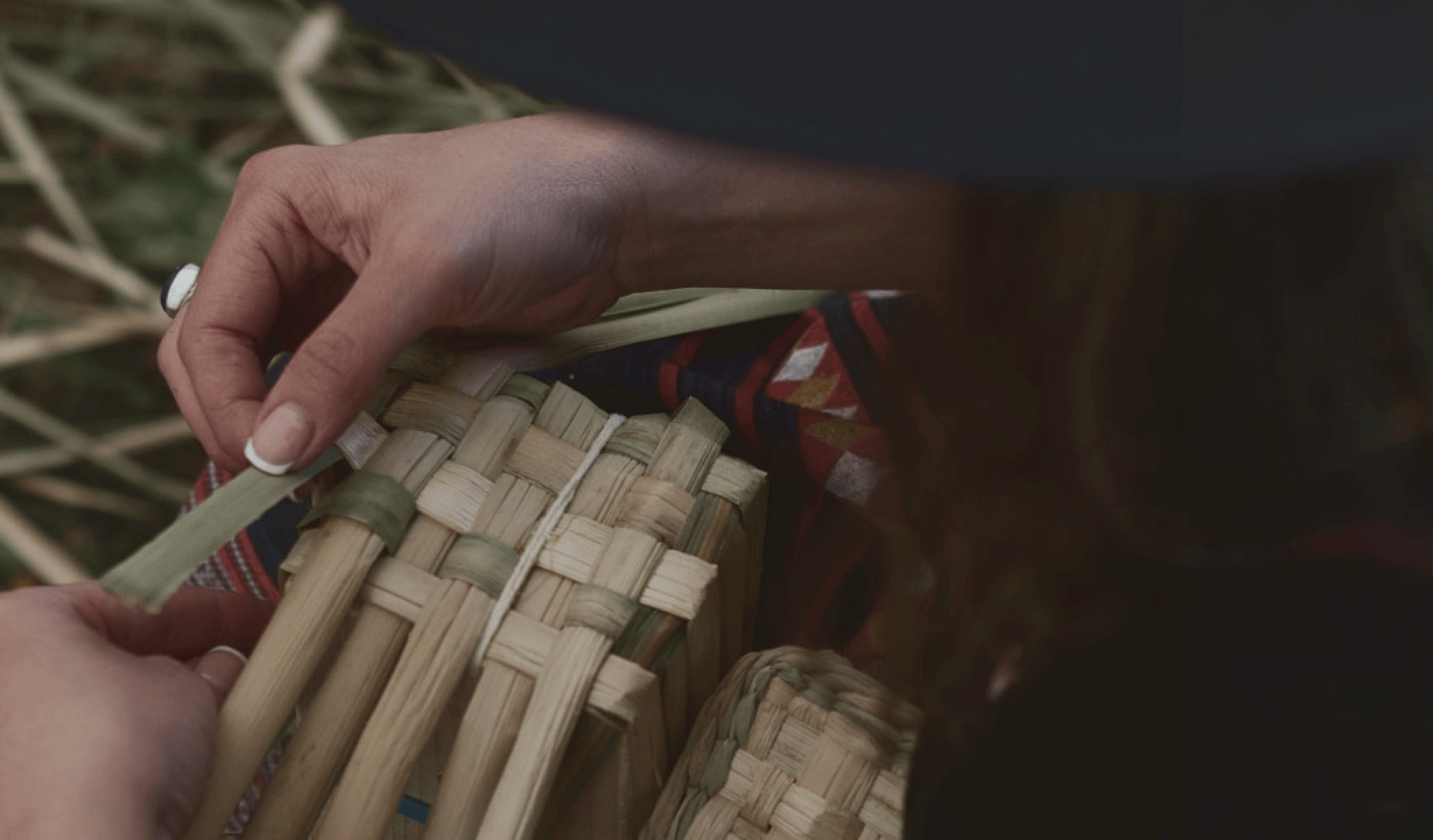 Close-up of hands weaving a basket with cattail leaves