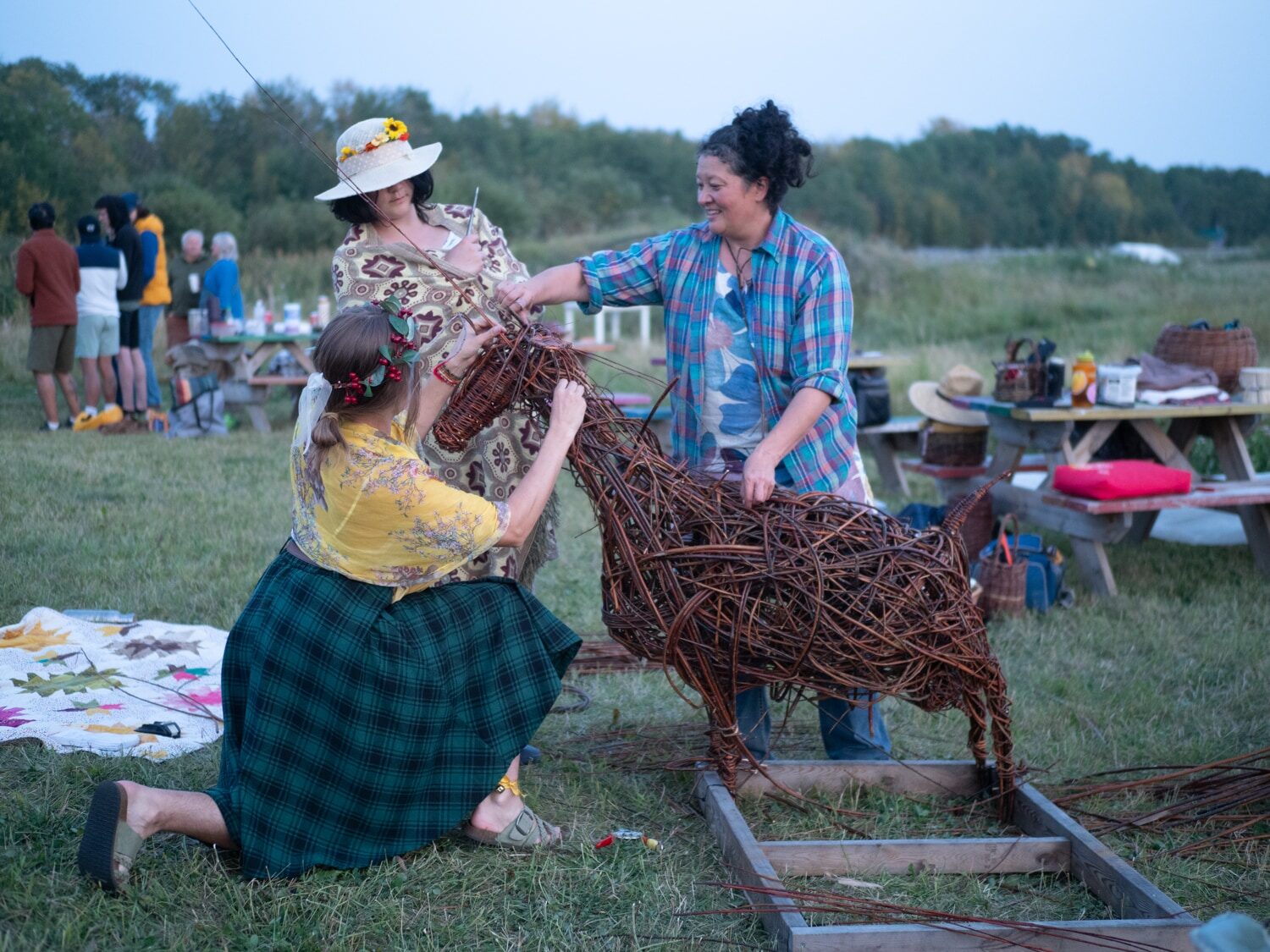 Two people fitting the head onto a large woven willow goat at dusk