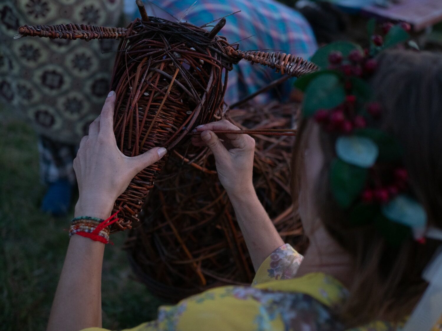 Close hands weaving the willow goat's head, a berry crown nearby